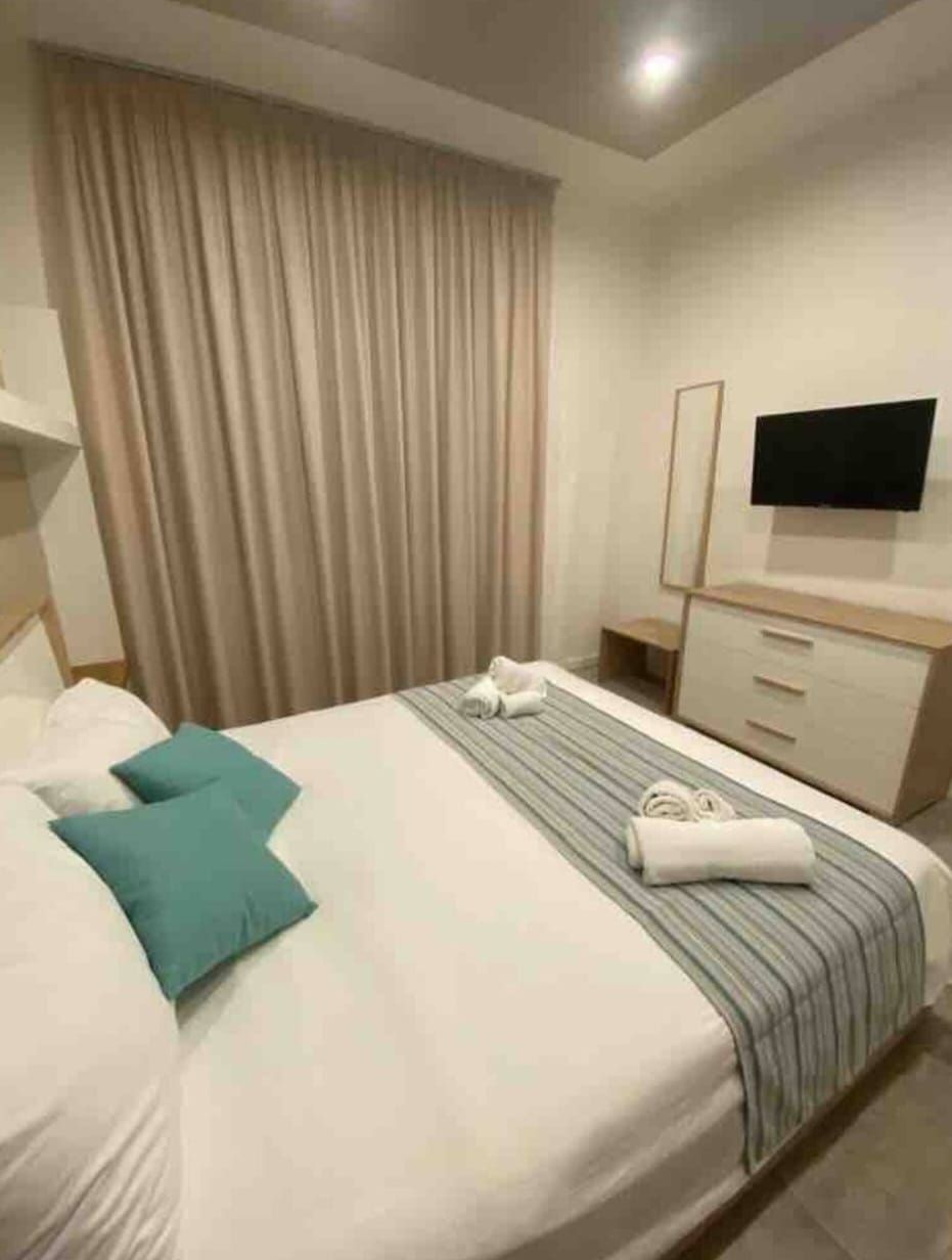 Una camera d'albergo con un letto, una televisione, un comò e una finestra con tende.