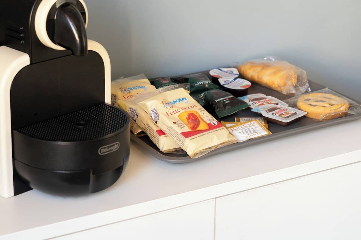 A coffee machine dispensing coffee into a cup, with a tray of packaged food items and a wrapped pastry on a counter.