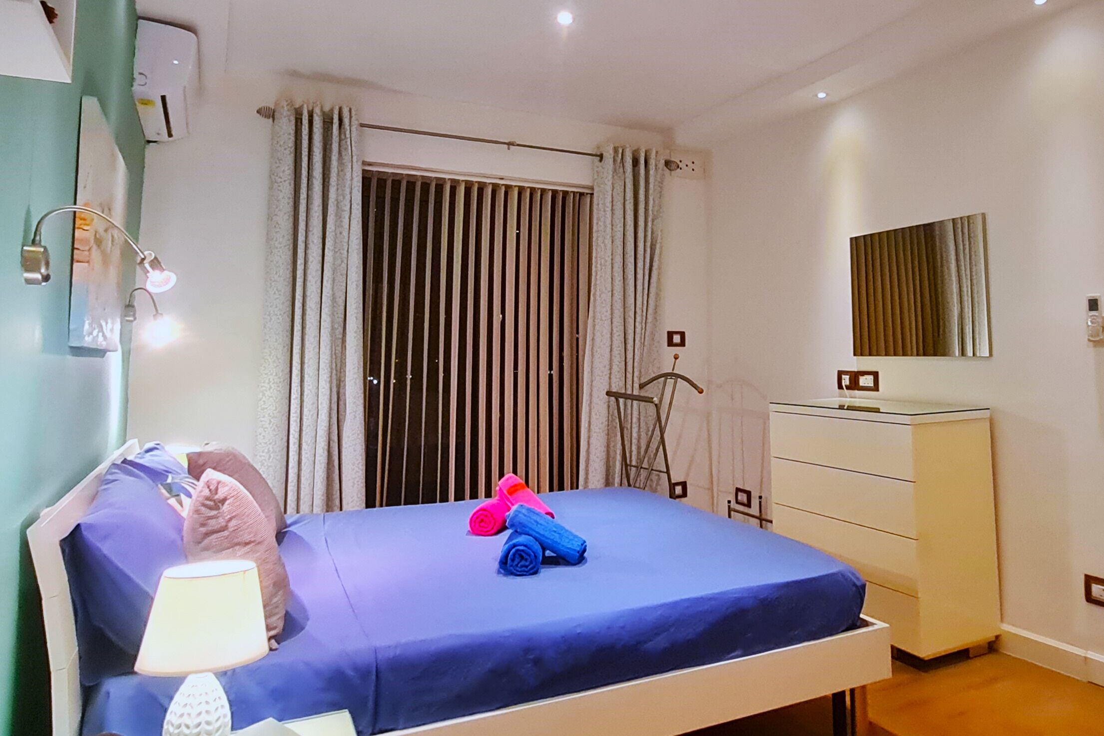 Une chambre à coucher avec un lit, une commode, un miroir et une fenêtre avec des rideaux.