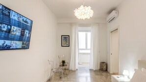 A modern hotel room with a large digital photo collage on the wall, a patterned bedspread, a clear glass table with a vase of flowers, and a view of the outside through a large window. - Via Veneto Home (Roma)
