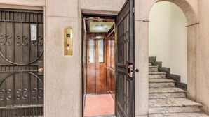 An elevator entrance with a metal door, a control panel, and a marble staircase leading to an upper floor. - Via Veneto Home (Roma)