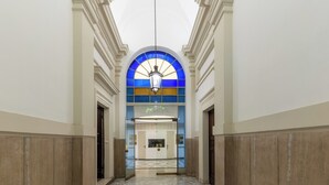 A hallway with a tiled floor, a central elevator, and a large arched window with blue and yellow panes. - Via Veneto Home (Roma)