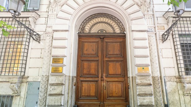 A large wooden double door with a decorative arch above it, set in a building with ornate architectural details. - Via Veneto Home (Roma)