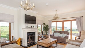 A spacious living room with a fireplace, a large flat-screen TV, and a comfortable seating area with a view of the outdoors. - 5 Bed Villa - Sleeps 10 - Hot Tub - Country Views (Ardmore)