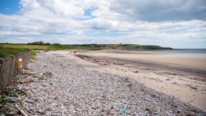 A pebbled beach with a wooden fence and a distant view of a house. - 5 Bed Villa - Sleeps 10 - Hot Tub - Country Views (Ardmore)