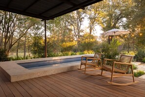 A wooden deck with a hot tub, two rocking chairs, and an umbrella.