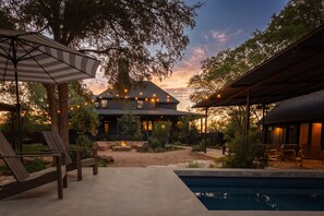 A pool area with lounge chairs, a fire pit, and a house in the background.