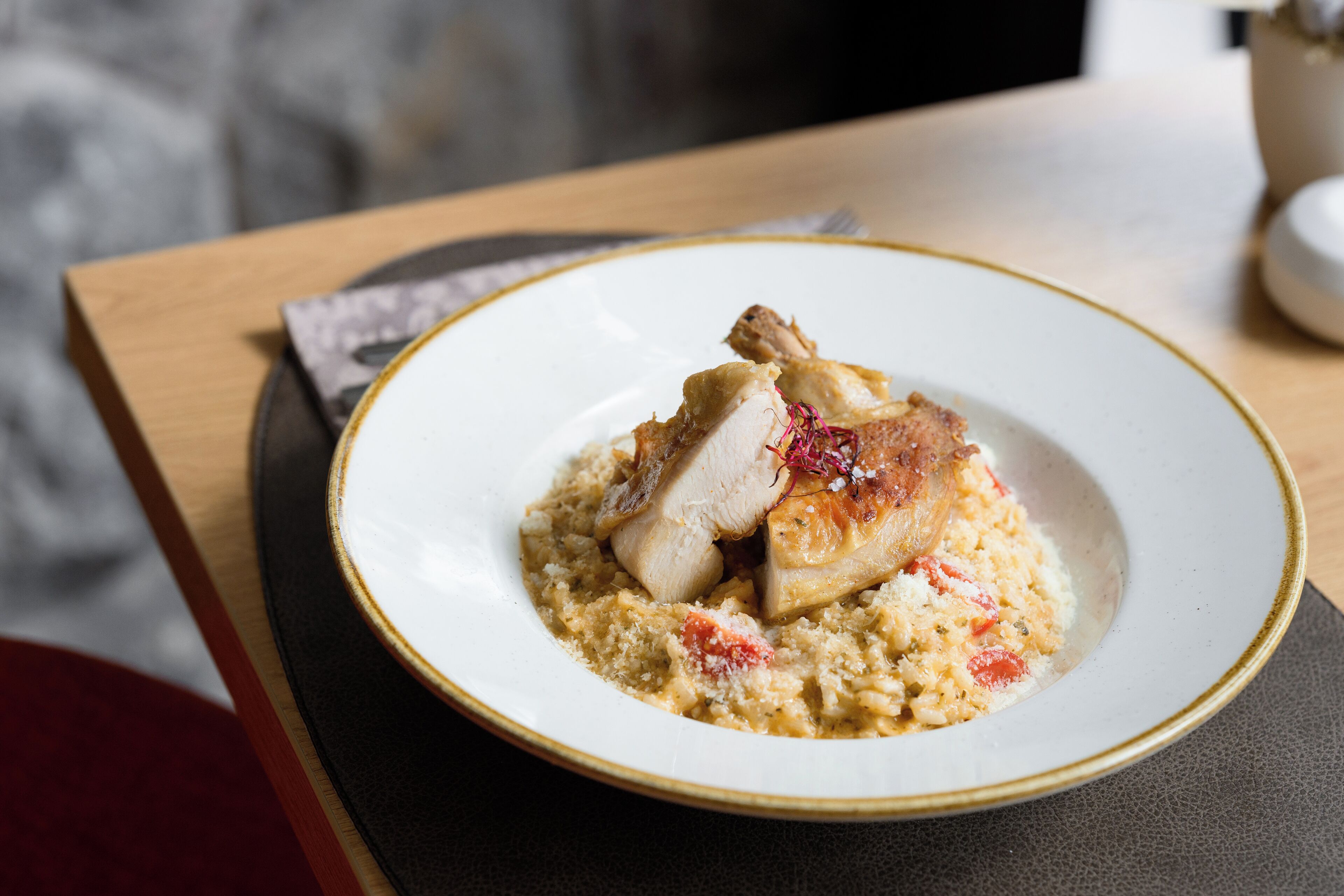 En tallerken mad med et stykke kød og en cremet bund, muligvis risotto, på en hvid tallerken med guld kant.
