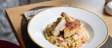 A plate of food with a piece of meat and a creamy base, possibly a risotto, on a white plate with a gold rim.