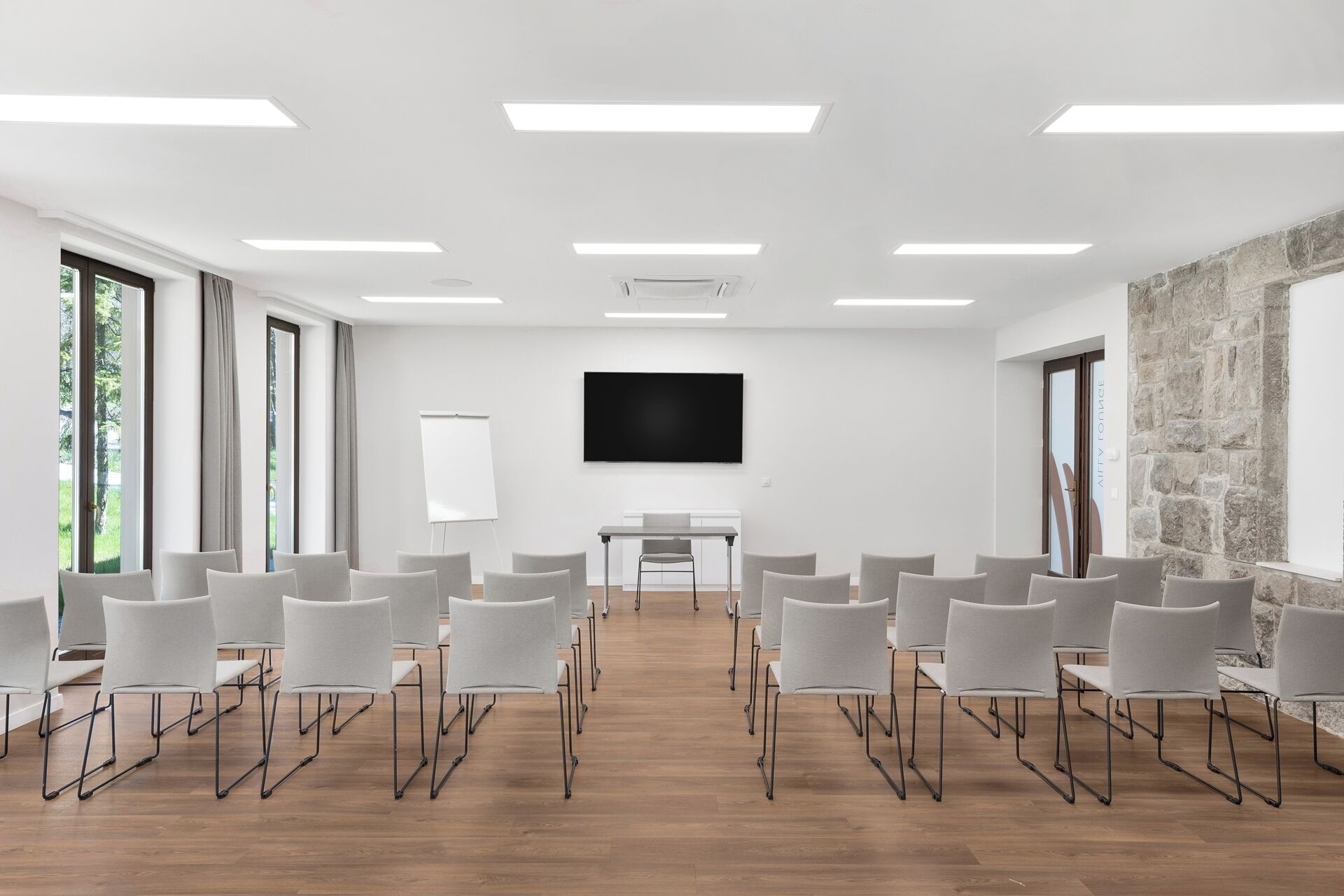 Uma sala de conferências com uma grande televisão de tela plana, cadeiras brancas, um quadro branco e uma parede de pedra decorativa.