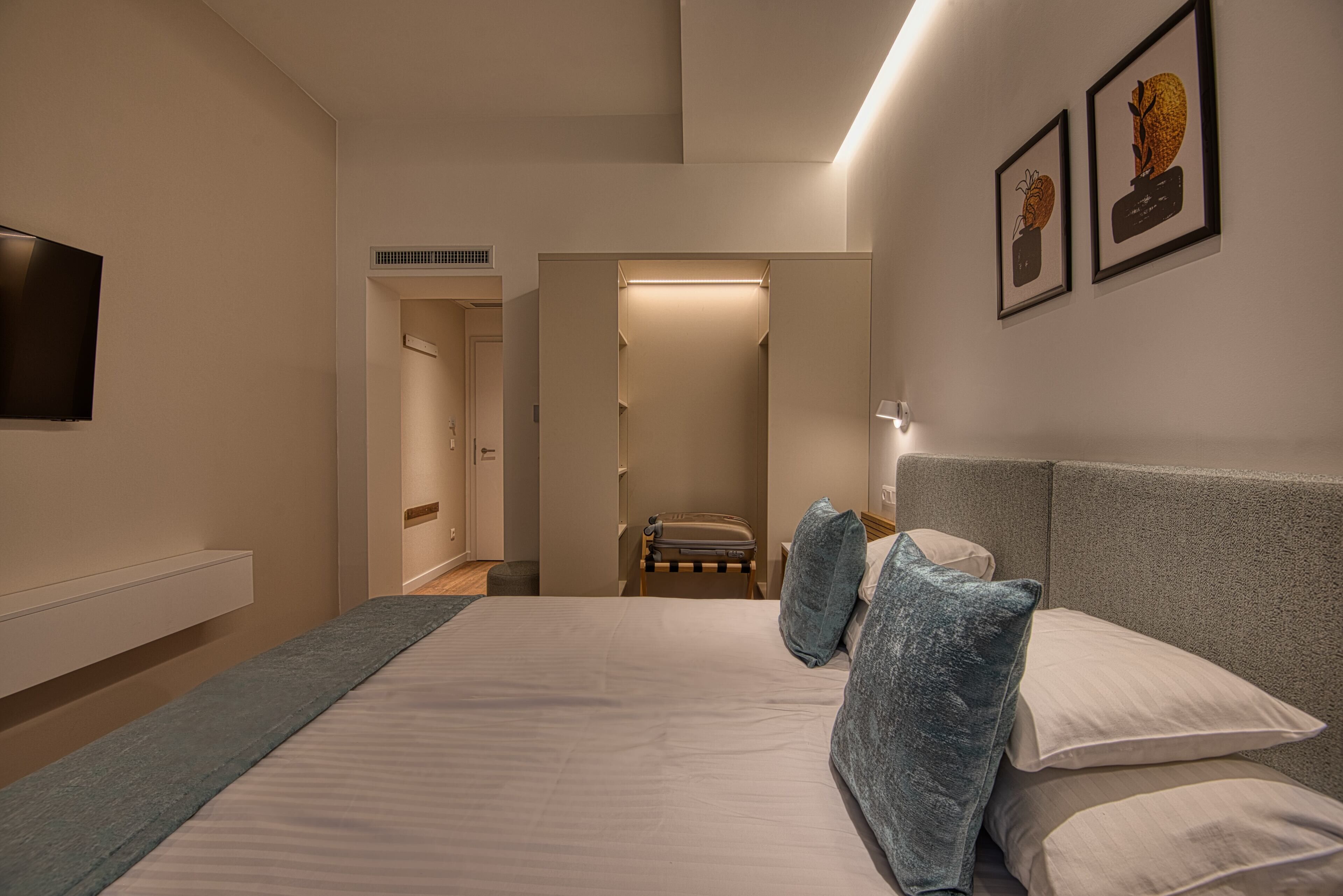 Un dormitorio moderno con cama, almohadas, una mesita de noche, televisor y cuadros en la pared.