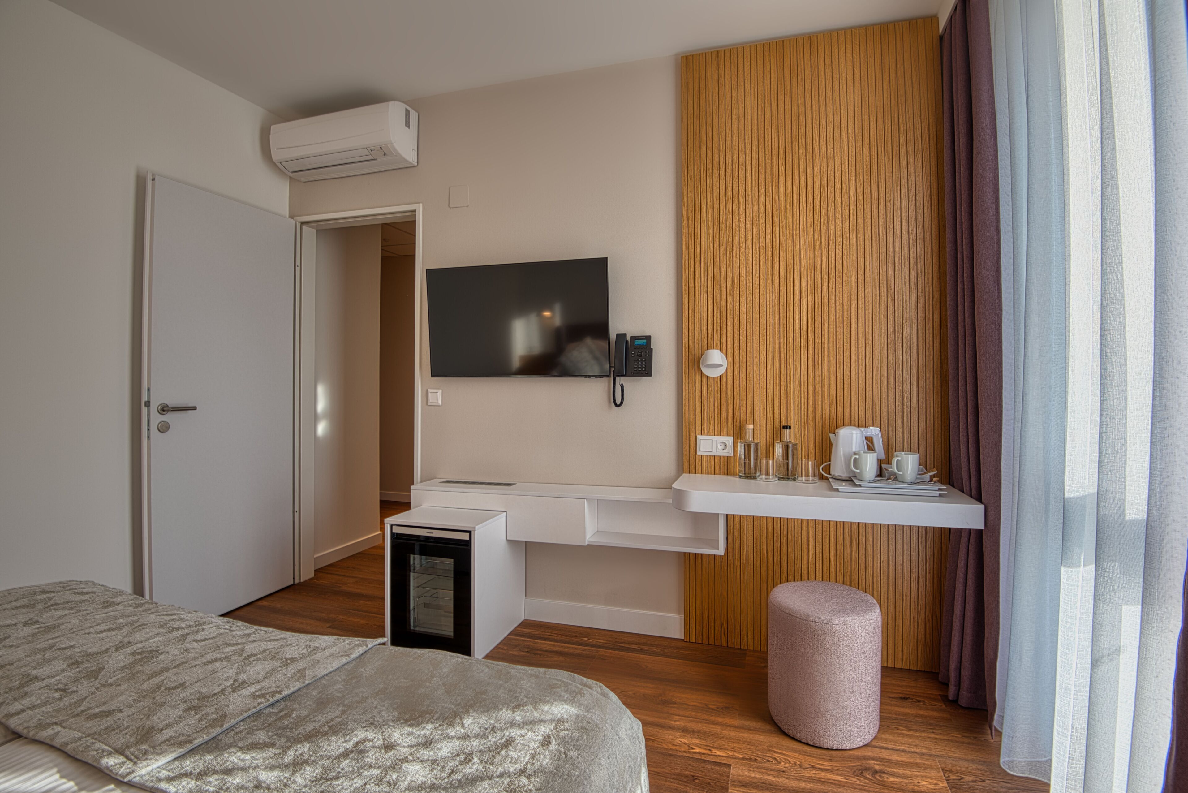 Una habitación de hotel moderna con cama, escritorio con televisor de pantalla plana, kitchenette pequeño y pared decorativa de madera.