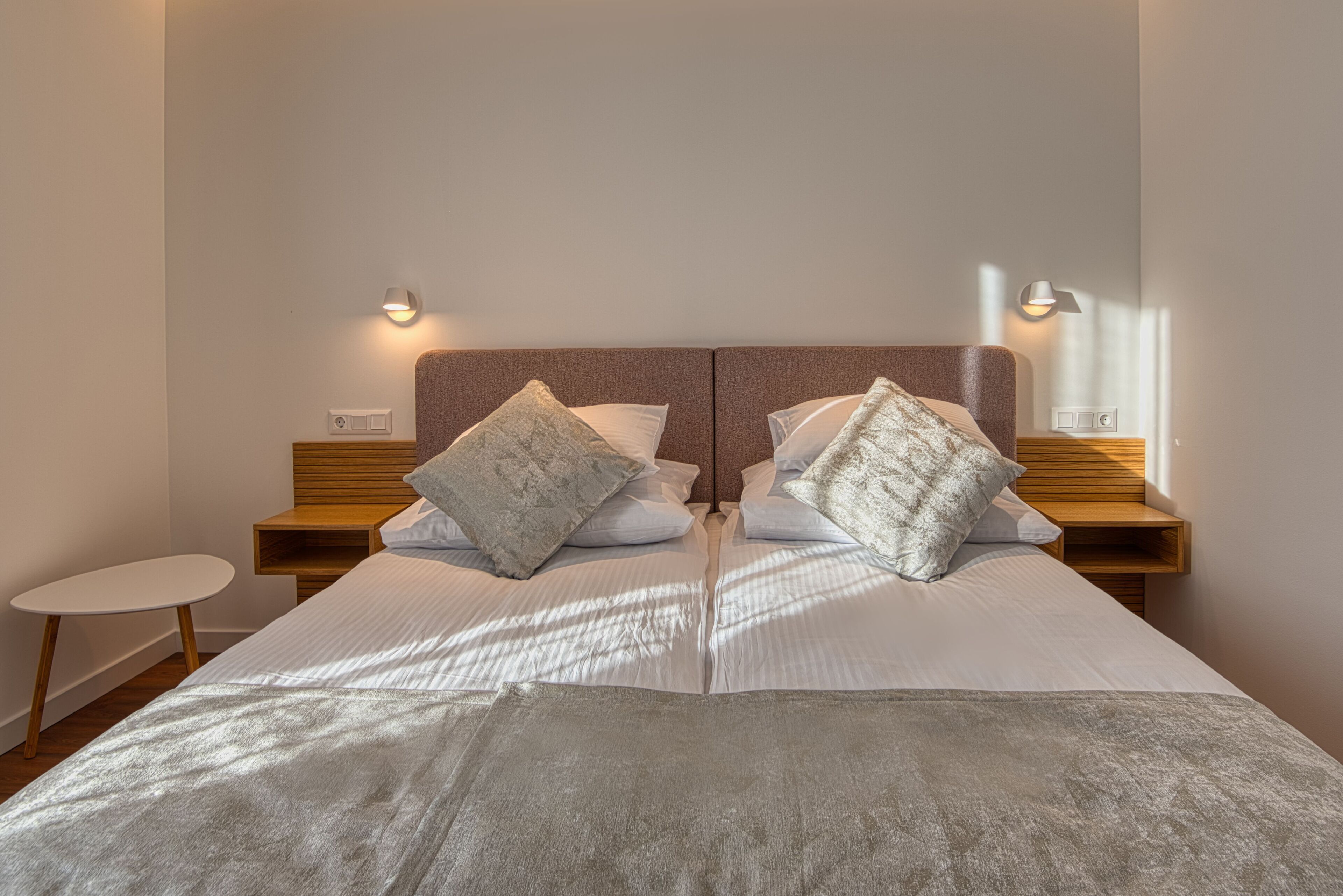 Una cama doble con cabecera de madera, dos mesitas de noche y una mesita auxiliar.