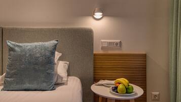 Habitación de hotel con cama, mesita de noche con frutas, luz de pared y toma de corriente.