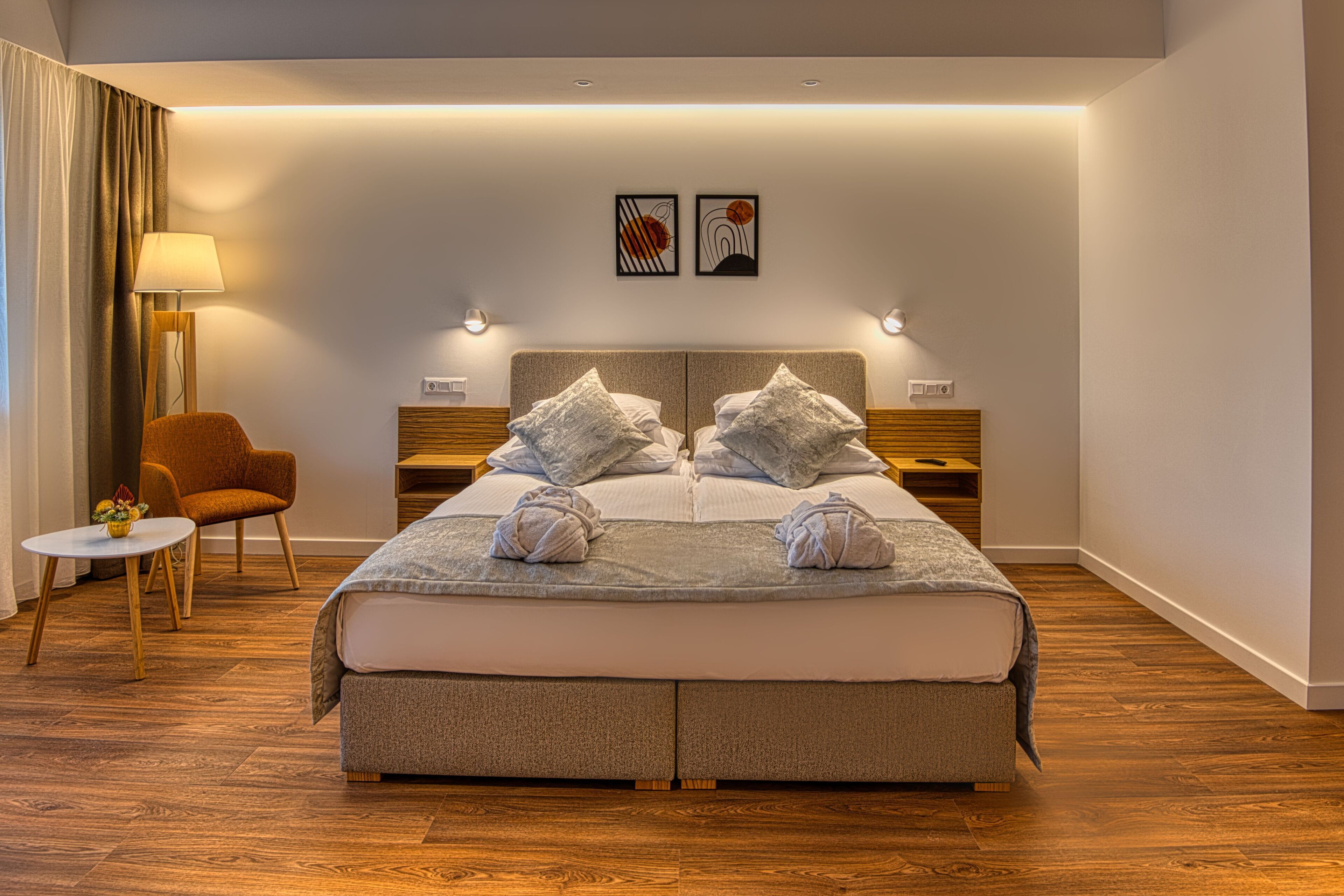 A modern hotel room with a large bed, two bedside tables, a chair, and a small table with a lamp.