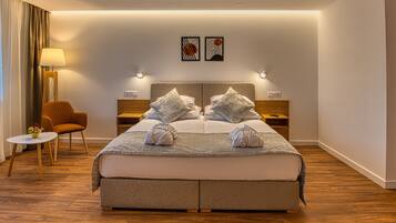 A modern hotel room with a large bed, two bedside tables, a chair, and a small table with a lamp.