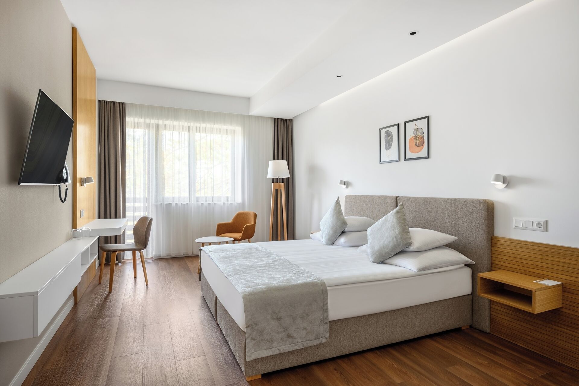 A modern hotel room with a large bed, a desk, a chair, and a TV.