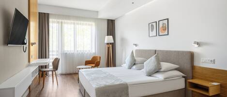 A modern hotel room with a large bed, a desk, a chair, and a TV.