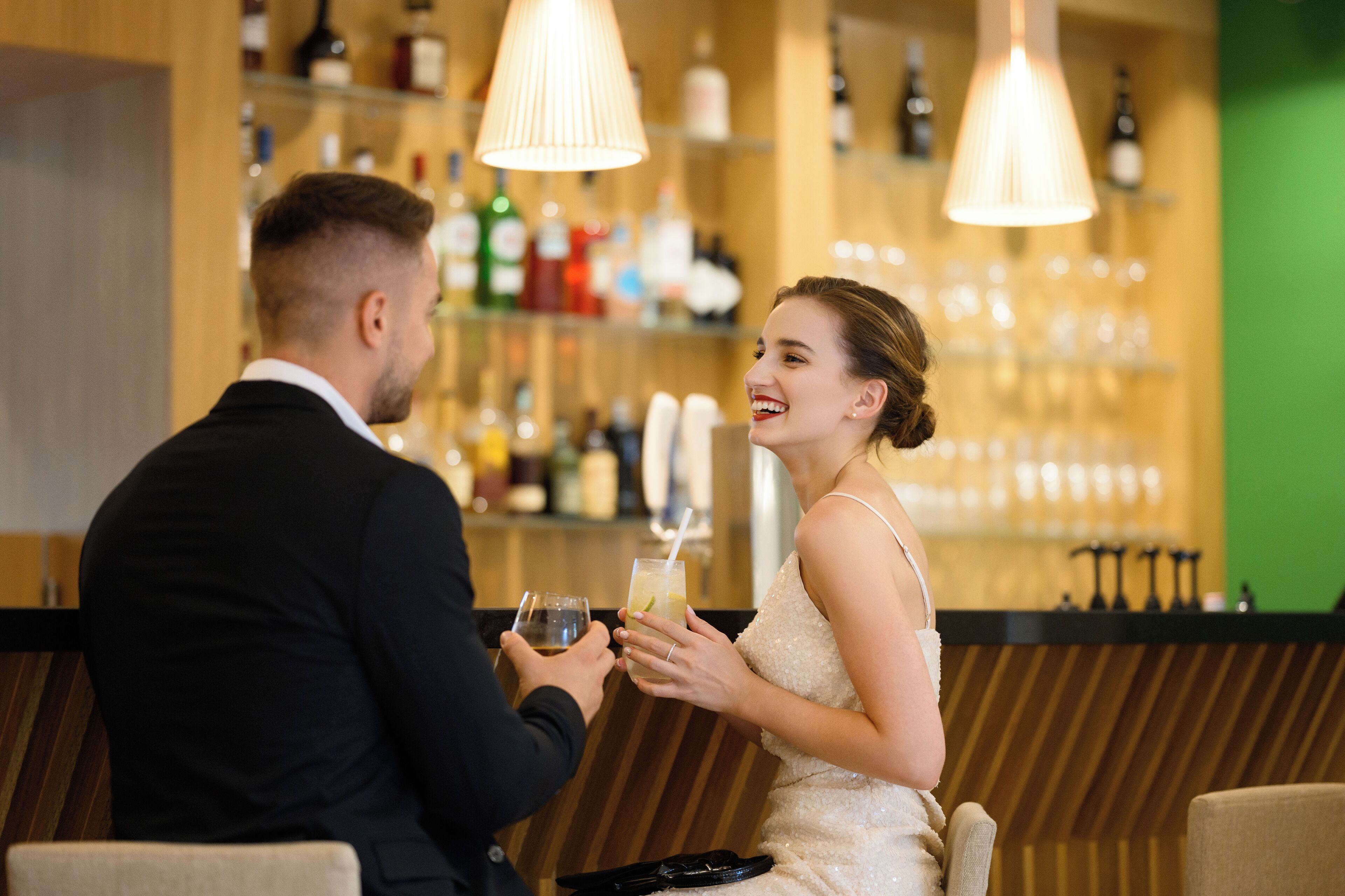 A couple seated at a bar with a variety of bottles and glasses in the background.