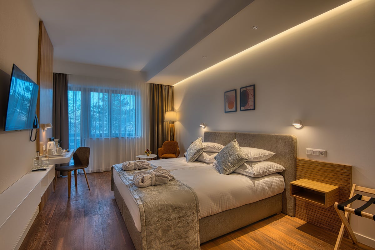 Ein modernes Hotelzimmer mit einem großen Bett, einem Schreibtisch, einem Sessel und einem an der Wand befestigten Fernseher.