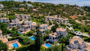 A residential area with multiple houses featuring Mediterranean architecture, surrounded by greenery and hills.