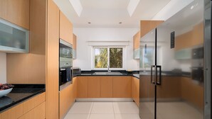 A modern kitchen with wooden cabinets, a stainless steel refrigerator, and a window with a view of greenery.