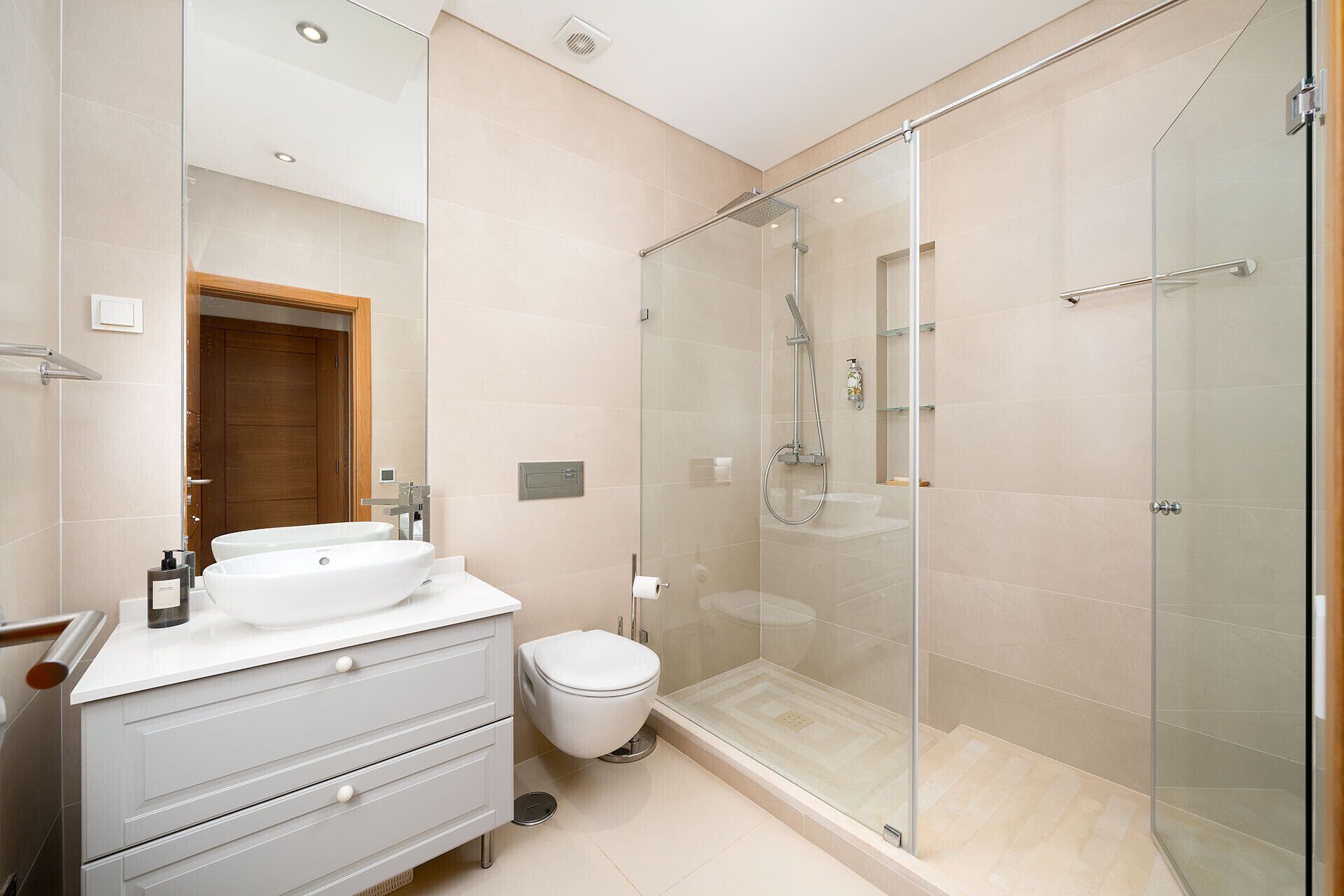 A modern bathroom with a glass-enclosed shower, a white sink, and a wooden door.
