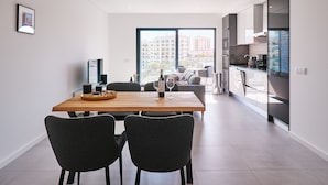 A modern kitchen with a large window, a dining area with a wooden table, and a view of a cityscape. - Terrace Daniel (Portimao)