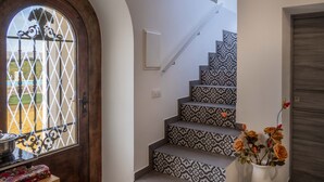 Un escalier avec des marches décorées, une porte en bois ornée d’une grille métallique et un vase rempli de fleurs.