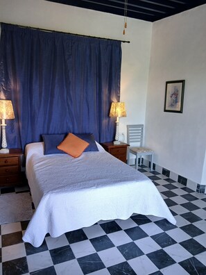 A neatly made bed with a white comforter, a blue curtain, two bedside lamps, a small bedside table with a lamp, and a checkered floor. - Tranquil rural Villa sleeps 5, Exclusive Private Pool, great views, close to sea (Vera)