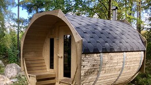 Un sauna en bois doté d’un toit incurvé, d’une porte et d’un banc à l’intérieur.