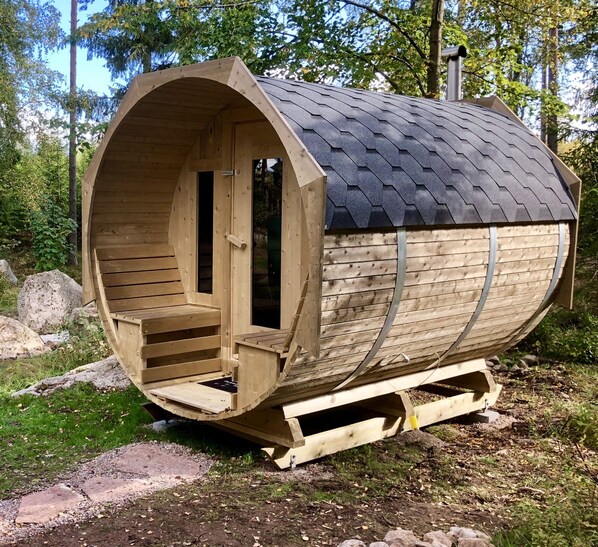Un sauna en bois doté d’un toit incurvé, d’une porte et d’un banc à l’intérieur.