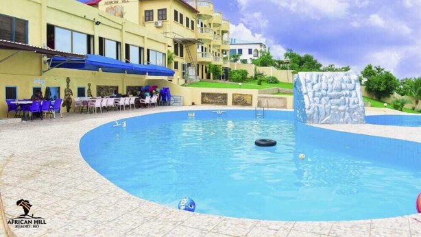 A pool area with a water slide, outdoor seating, and a building labeled "African Hill Resort." - African Hill Hotel & Resort (Ho)