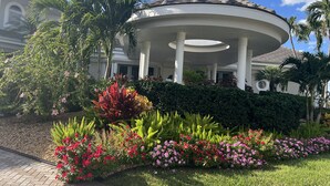 Un edificio con un'area coperta a forma circolare sostenuta da colonne, immerso nel verde e fiorito.