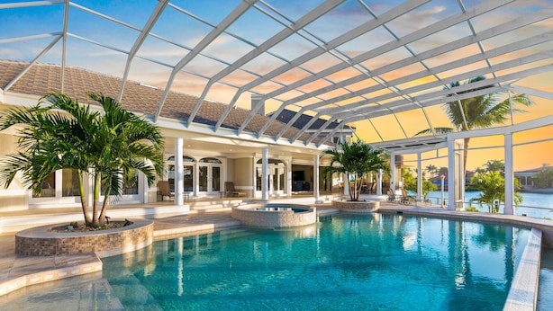 Area piscina con soffitto in vetro, palme e vista sull'oceano.