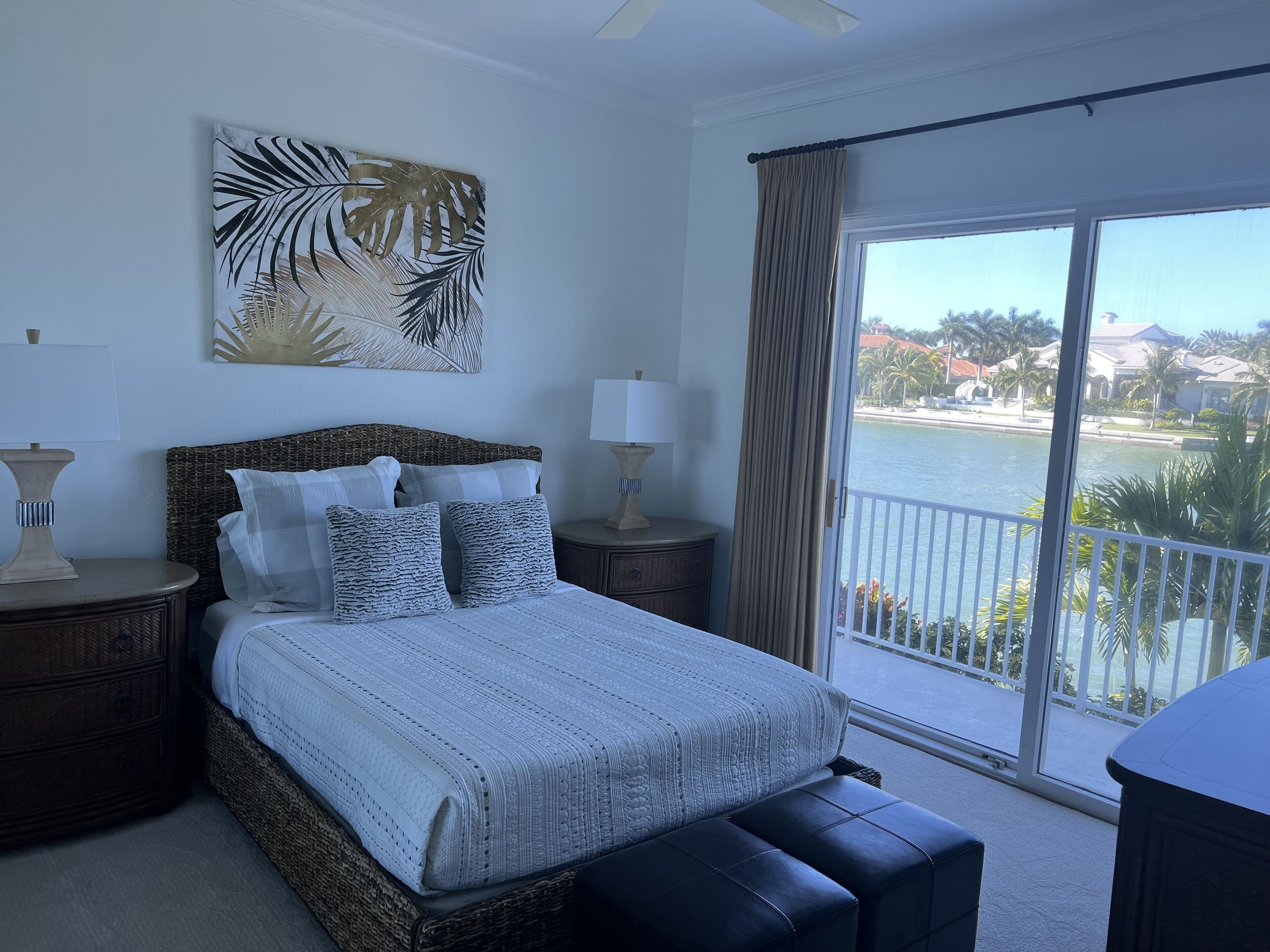 A bedroom with a large bed, two nightstands, a view of a body of water, and a balcony.