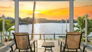 Una terrazza con due poltrone in vimini e un tavolino, affacciata su uno specchio d'acqua con vista sul tramonto.