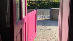A pink door leading to a balcony with a view of the sea and greenery.