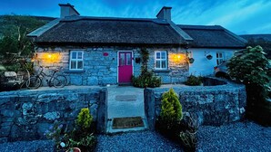 A stone house with a thatched roof, a pink door, and a bicycle parked outside.