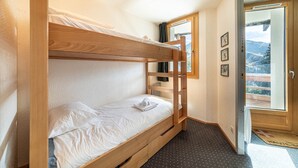 Een slaapkamer met stapelbed, een raam en een deur naar buiten.