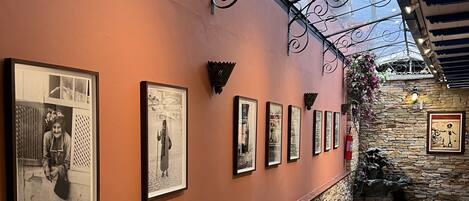 A corridor with framed photographs on the wall, a stone wall, and a tiled floor.