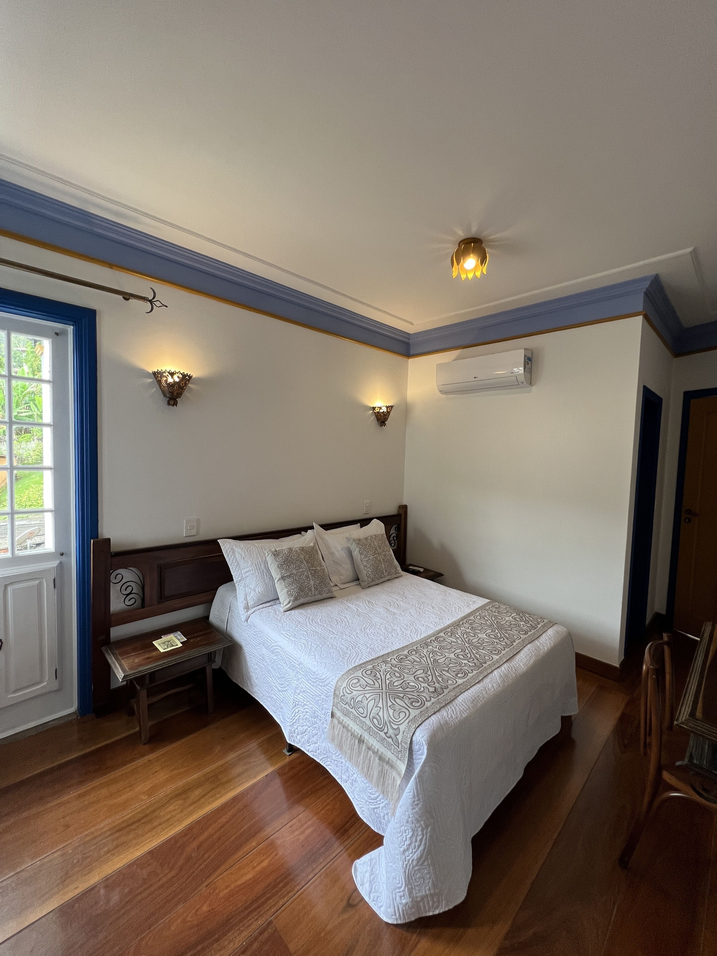Une chambre à coucher avec un lit en bois, deux appliques murales, un banc et une porte dotée d’un cadre bleu.