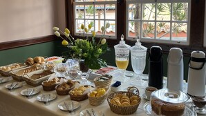 Une table de buffet garnie de divers plats et couverts, placée devant une fenêtre donnant sur un paysage verdoyant.