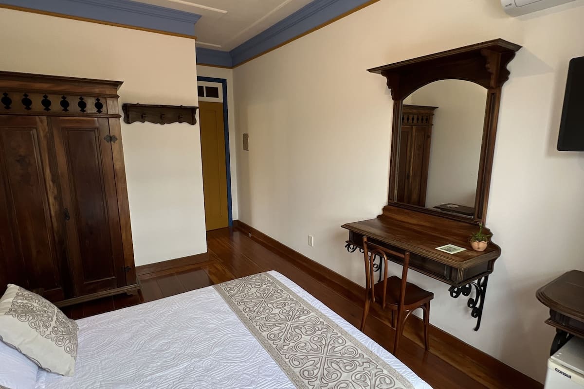 Un dormitorio con una cama grande, un escritorio de madera, un espejo y un armario.