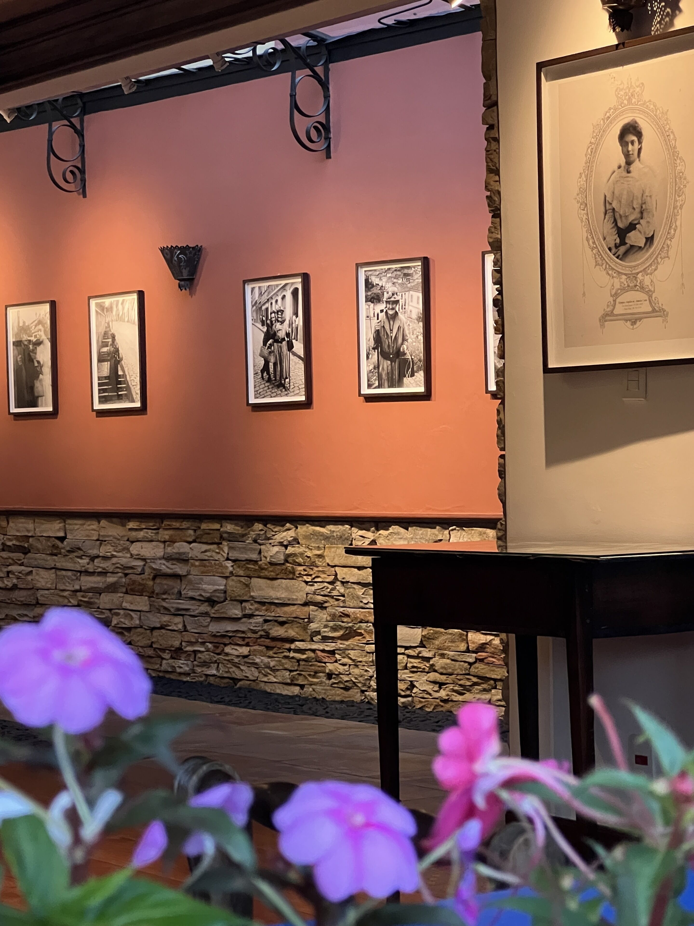 A wall with framed black and white photographs, a stone wall, and a table with a vase of flowers.