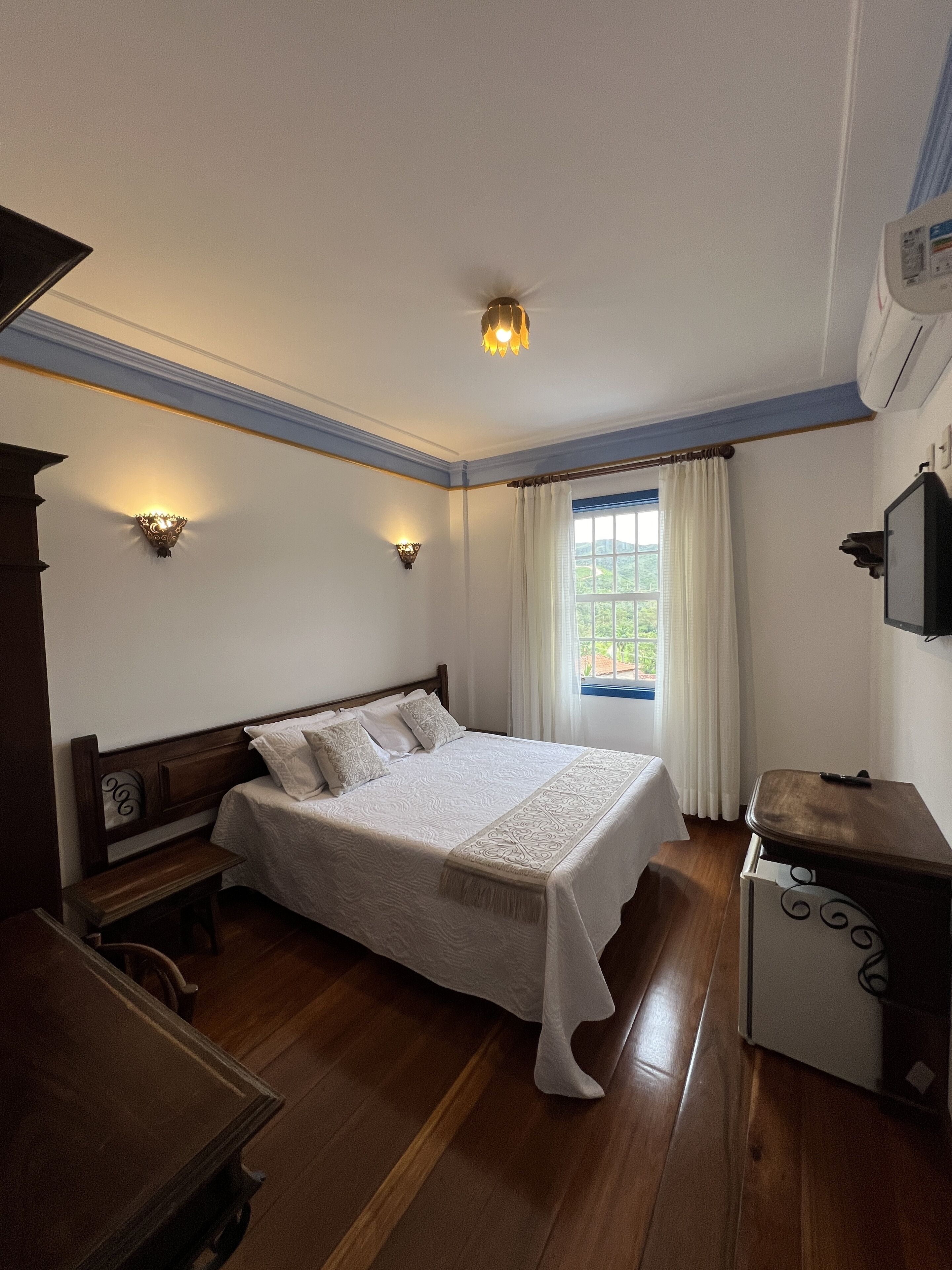 A neatly arranged bedroom with a large bed, bedside tables, a desk, and a window with curtains.