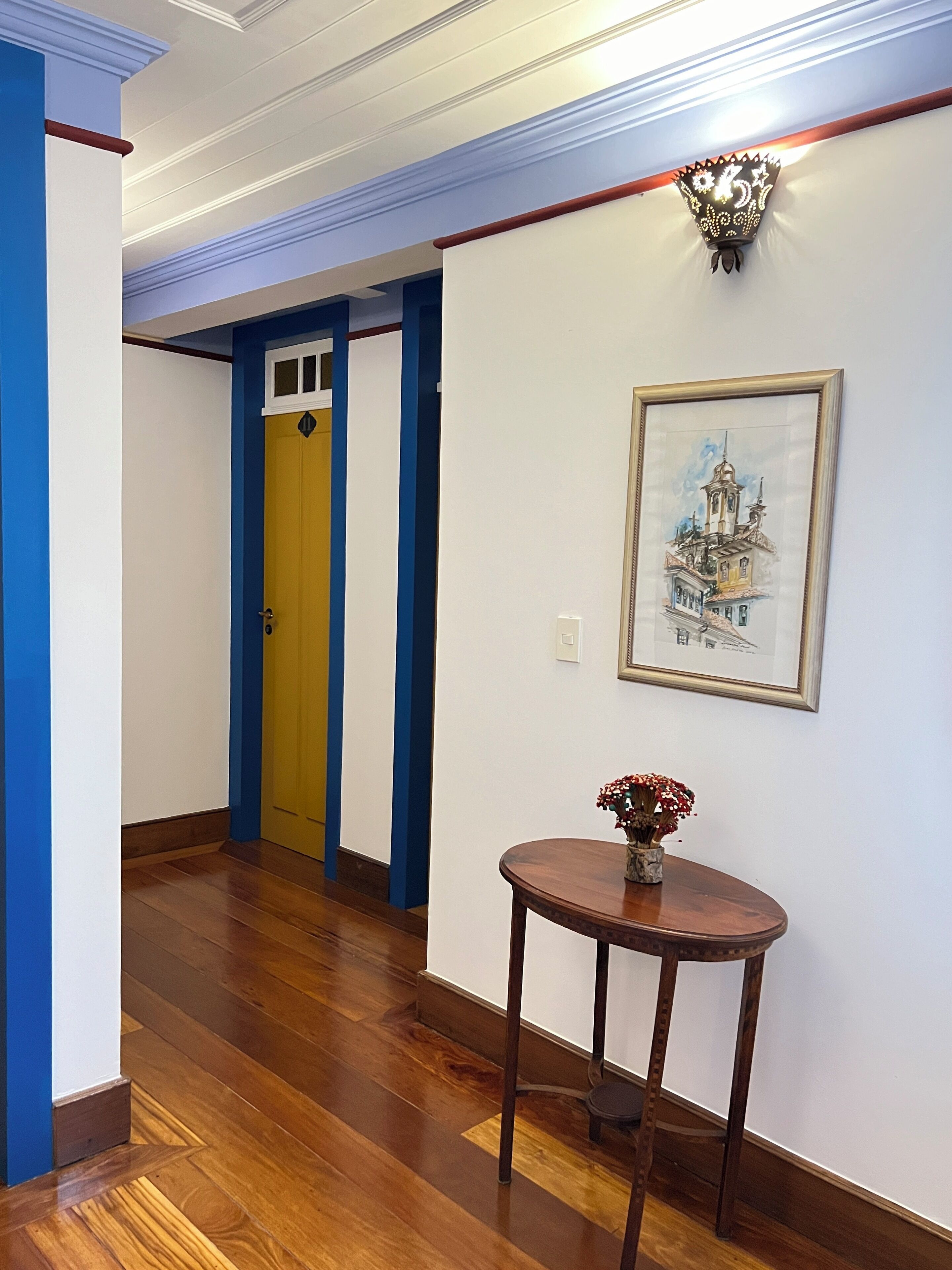 A hallway with wooden flooring, a yellow door, and a framed picture on the wall.