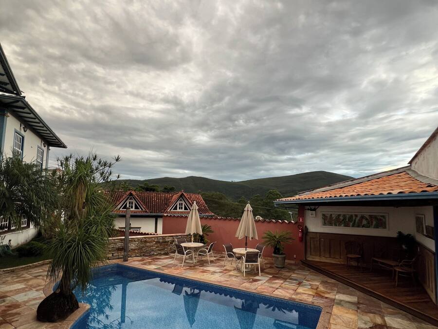 Piscina com deck ladrilhado, mobiliário de exterior e vista para colinas ao fundo.