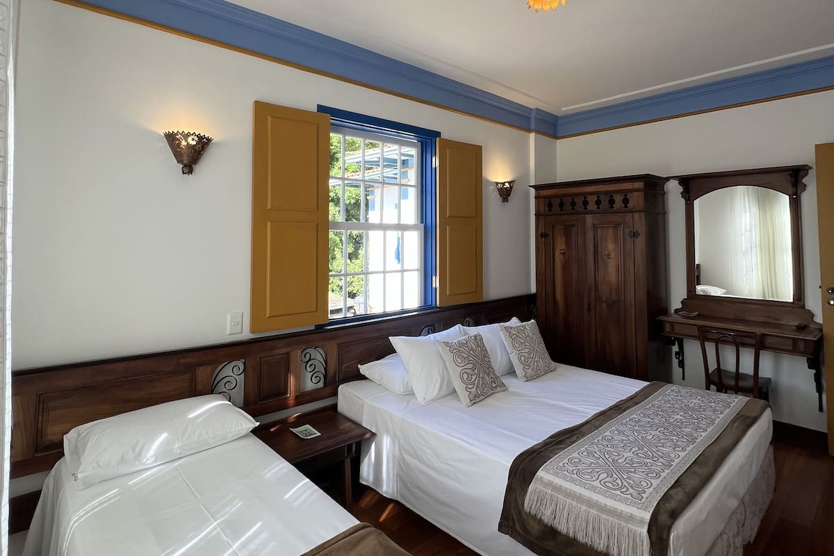 Una habitación de hotel con dos camas individuales, un escritorio de madera, un espejo y una ventana con contraventanas.