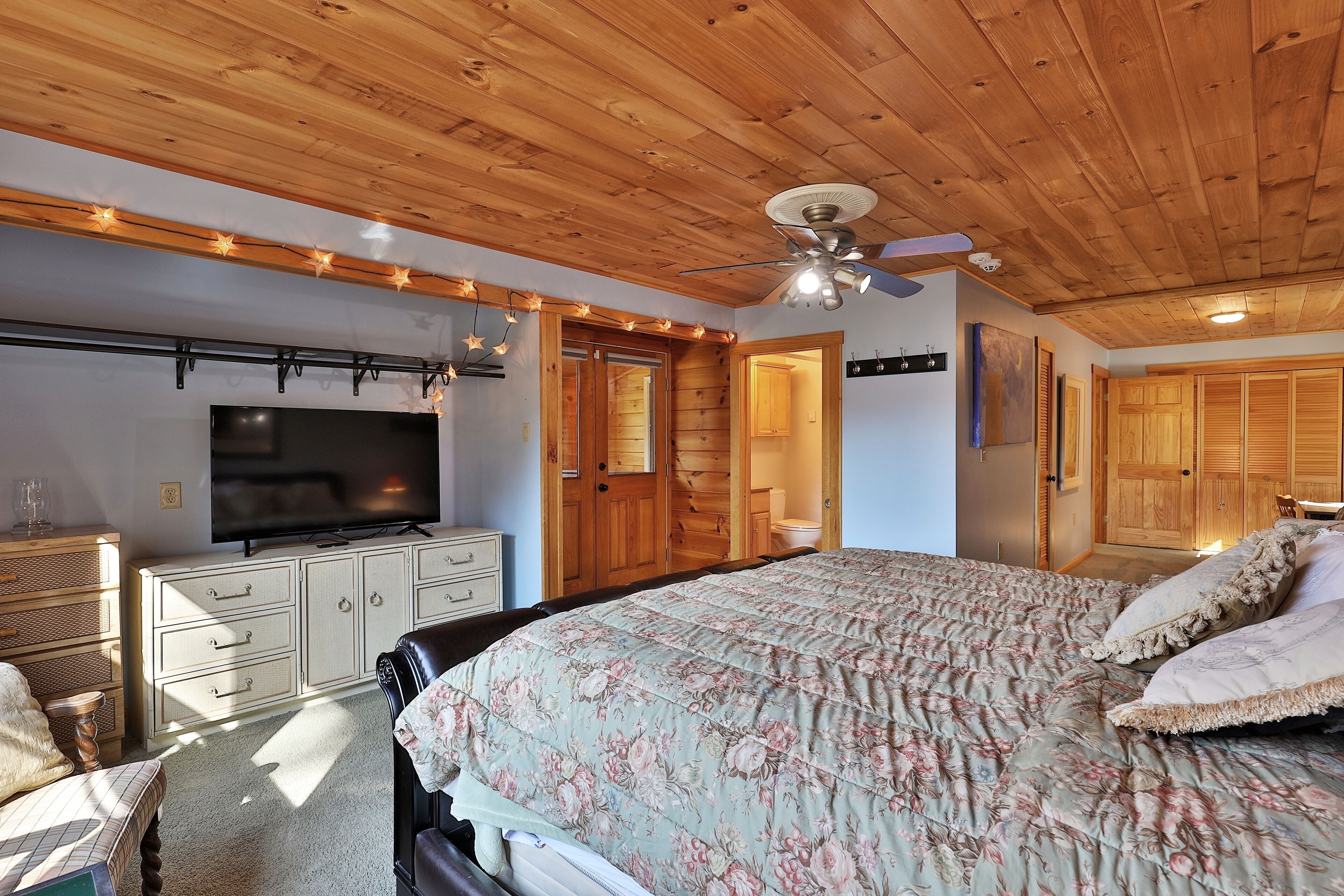 A bedroom with a wooden ceiling, a bed with floral bedding, a television, and a wardrobe.